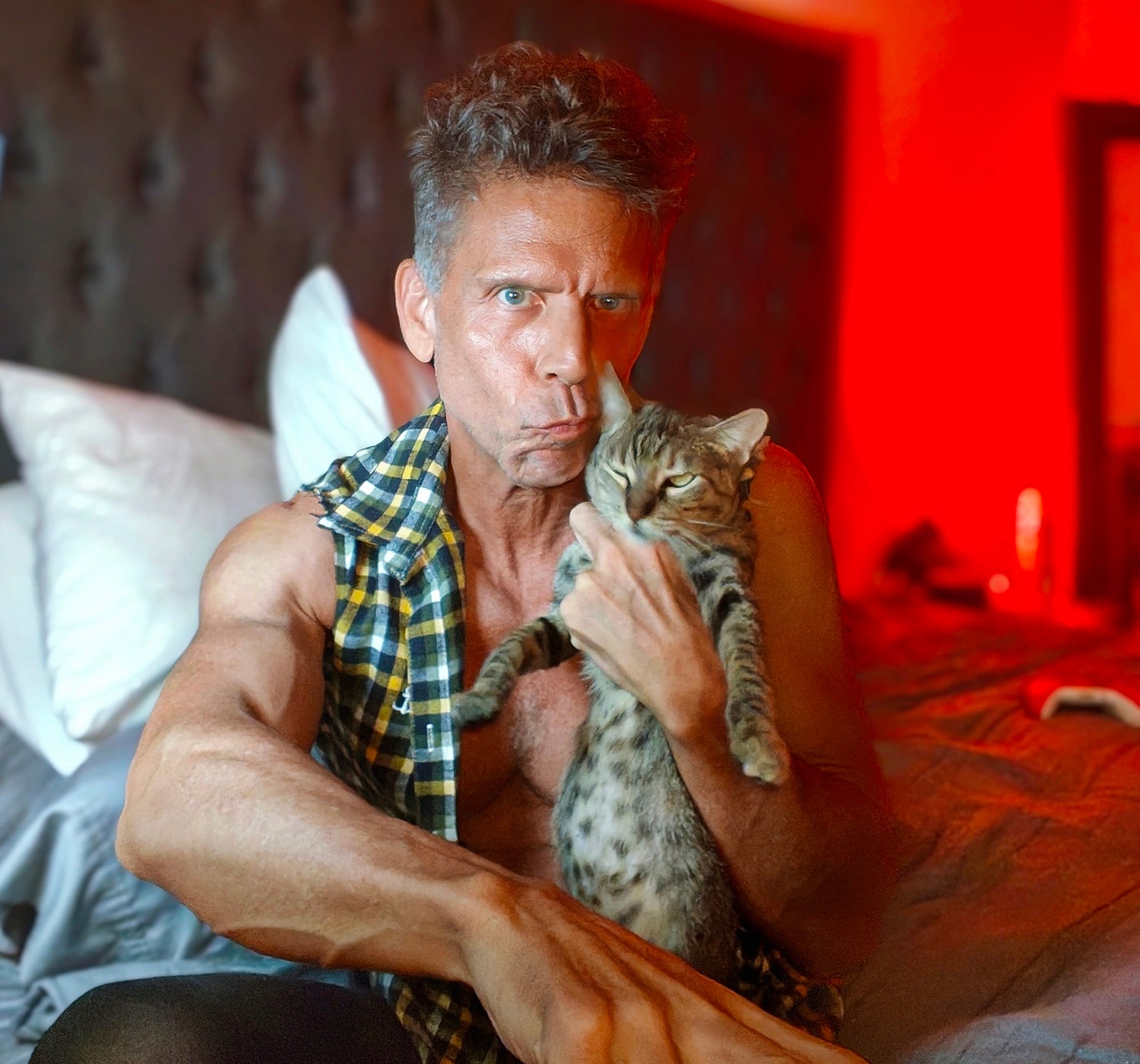 Eric holding a young cat he rescued named Carmens and sitting on a bed.